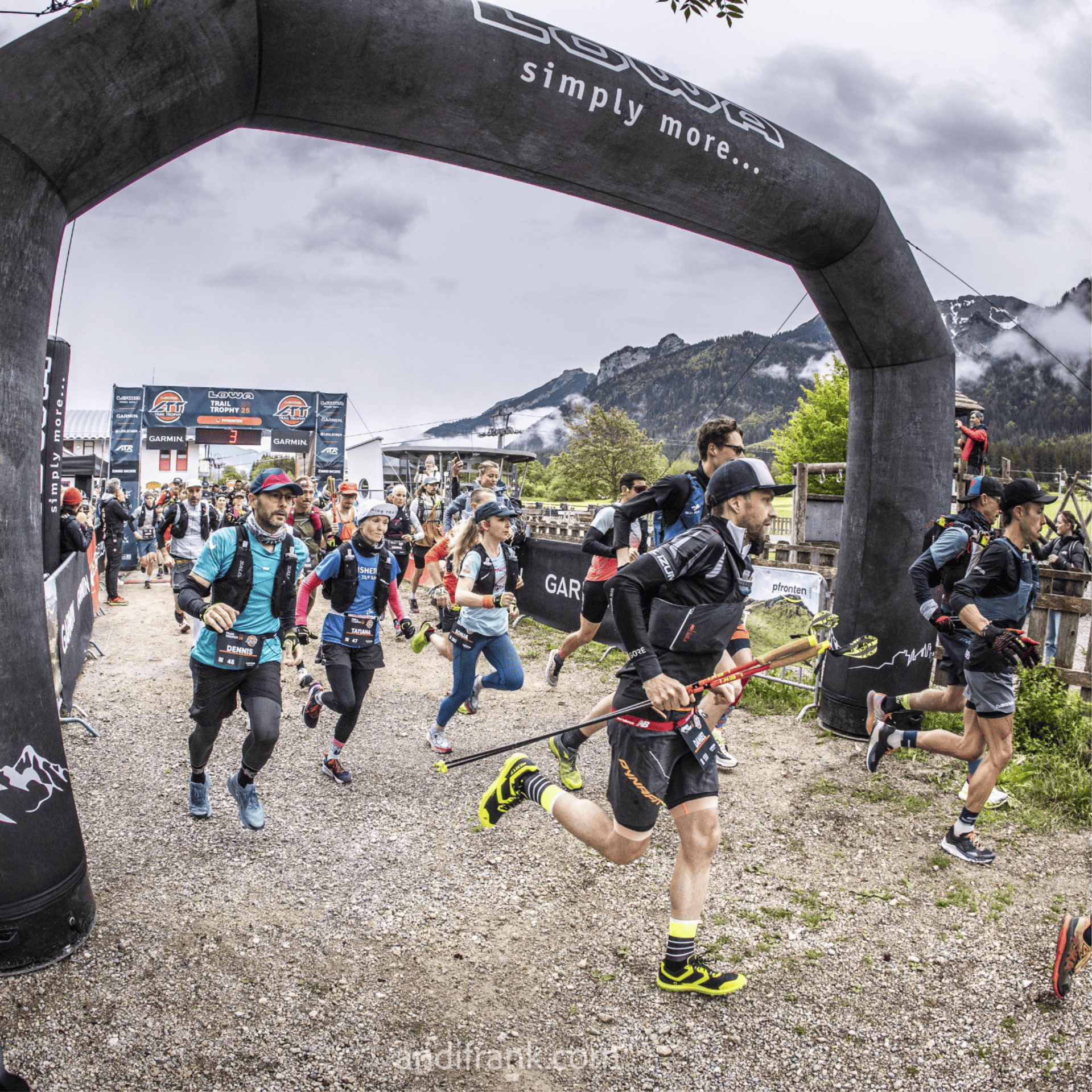 Runners pass under an archway, mountain scenery in the background.
