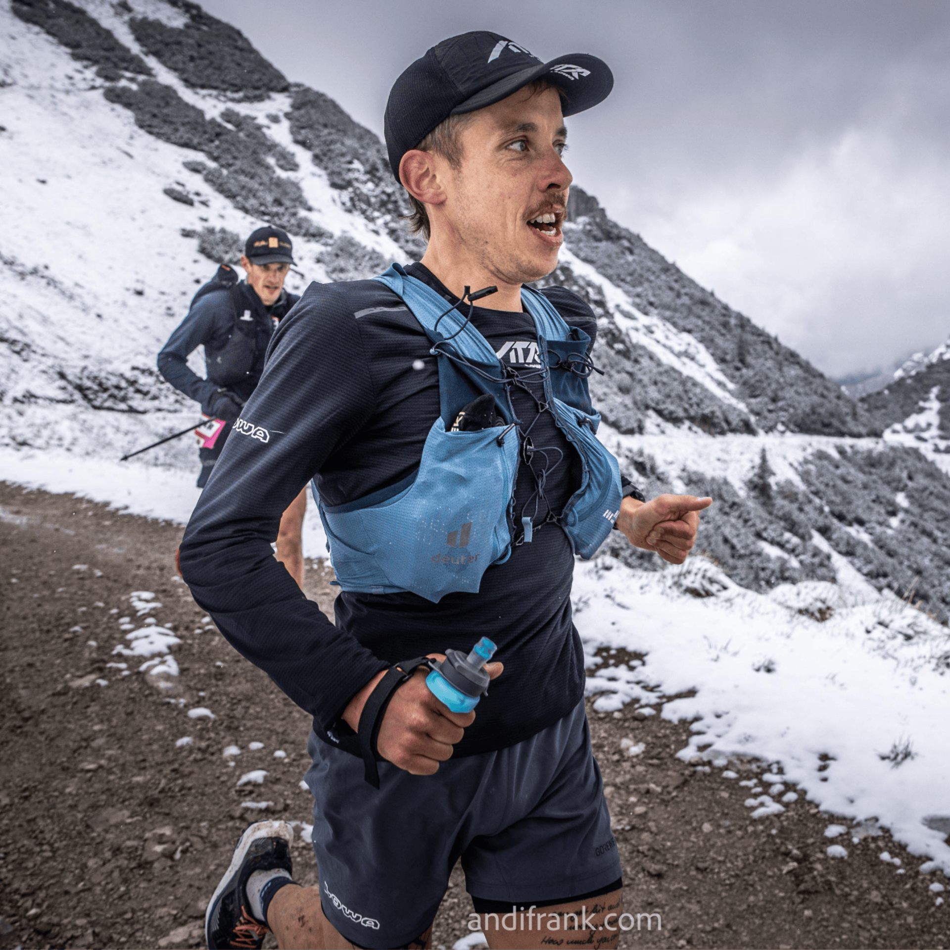 Trail runner with blue vest running in snow in the mountains.