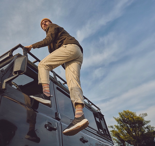 Three hikers on a mountain trail at sunset. One man in the foreground, two women in the background.