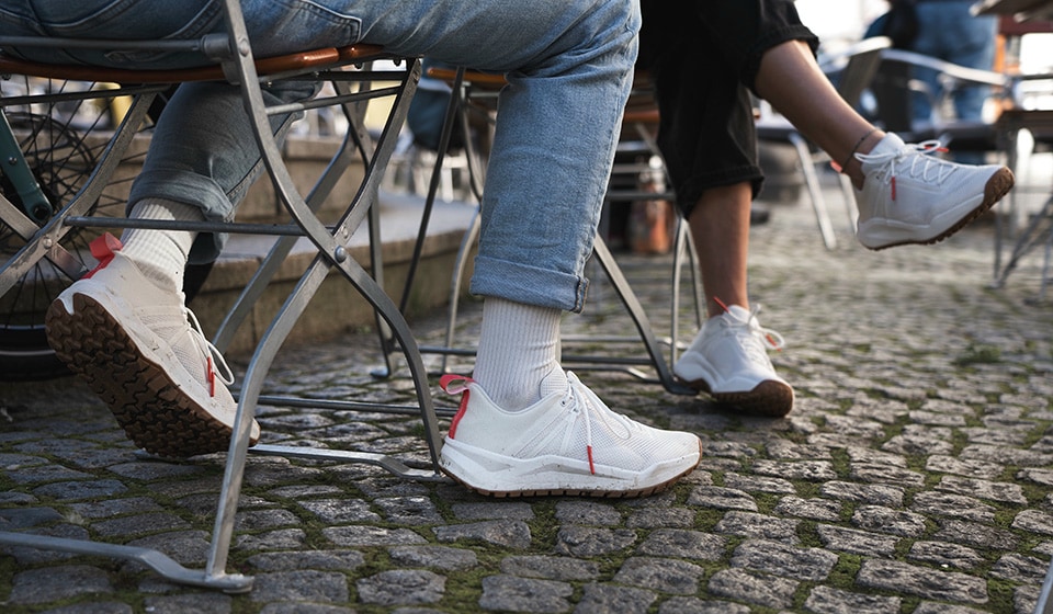 Feet of two people with running shoes on rocky ground with green vegetation.