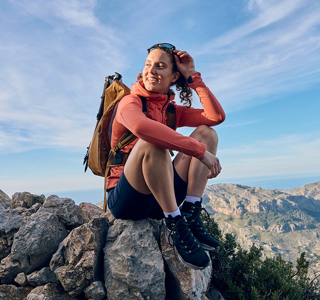 Female hiker with backpack sitting on a rock, looking at the mountains.