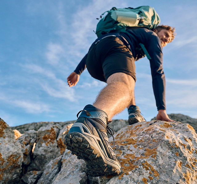 Man with hiking backpack climbing rocky terrain, focus on hiking boots.