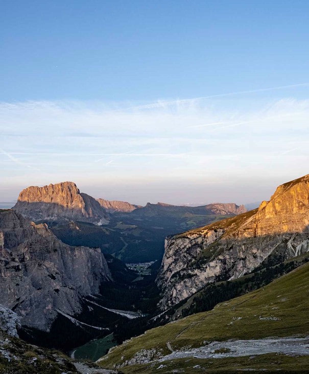 Pareti montuose illuminate dal sole e una profonda valle con un piccolo insediamento retroilluminato.