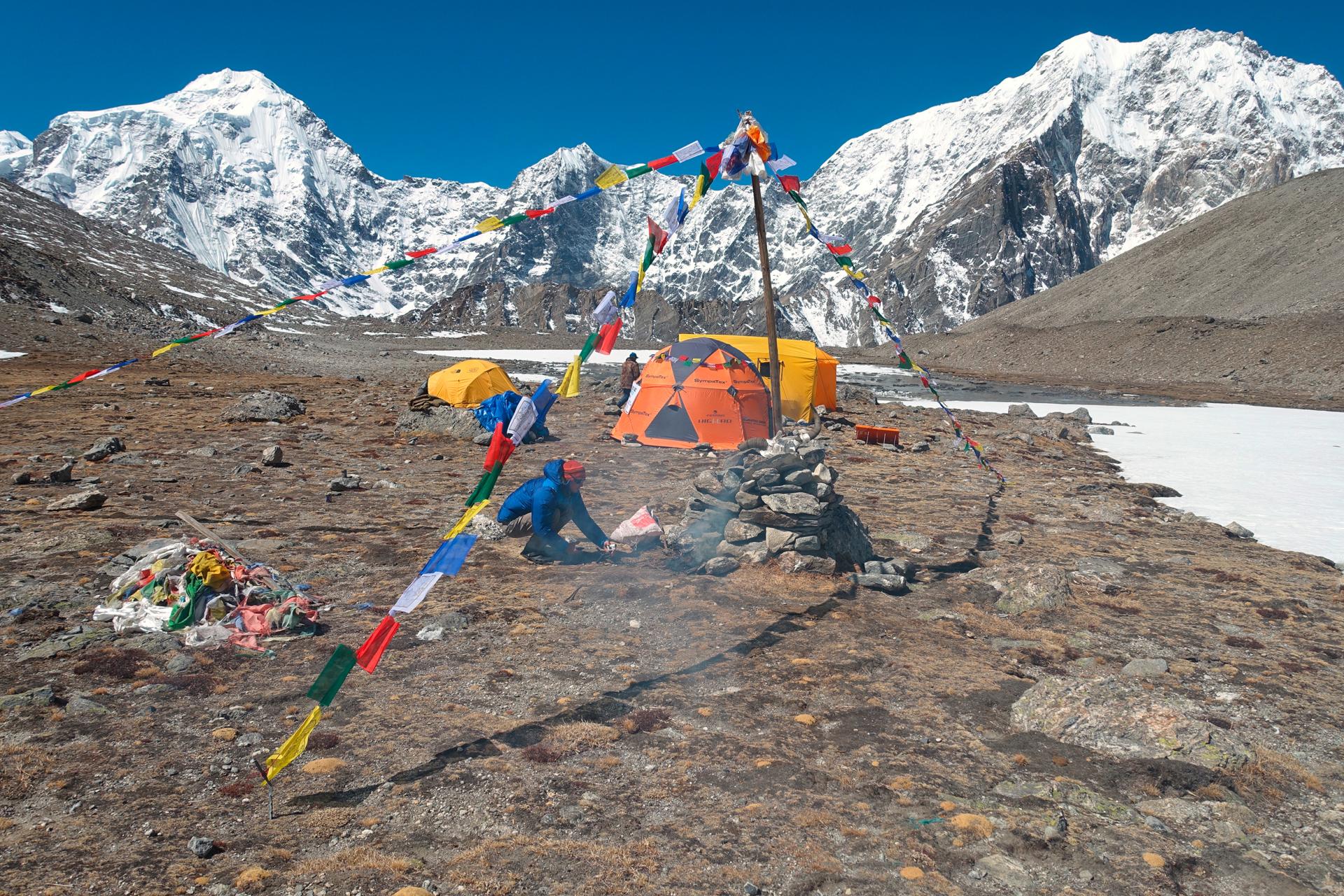 Bergsteiger-Camp mit Gebetsfahnen und Schnee bedeckten Bergen im Hintergrund.