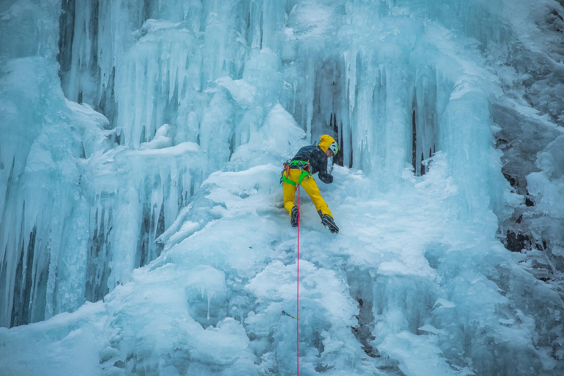 Ice climber in yellow clothes climbs at an icy waterfall.