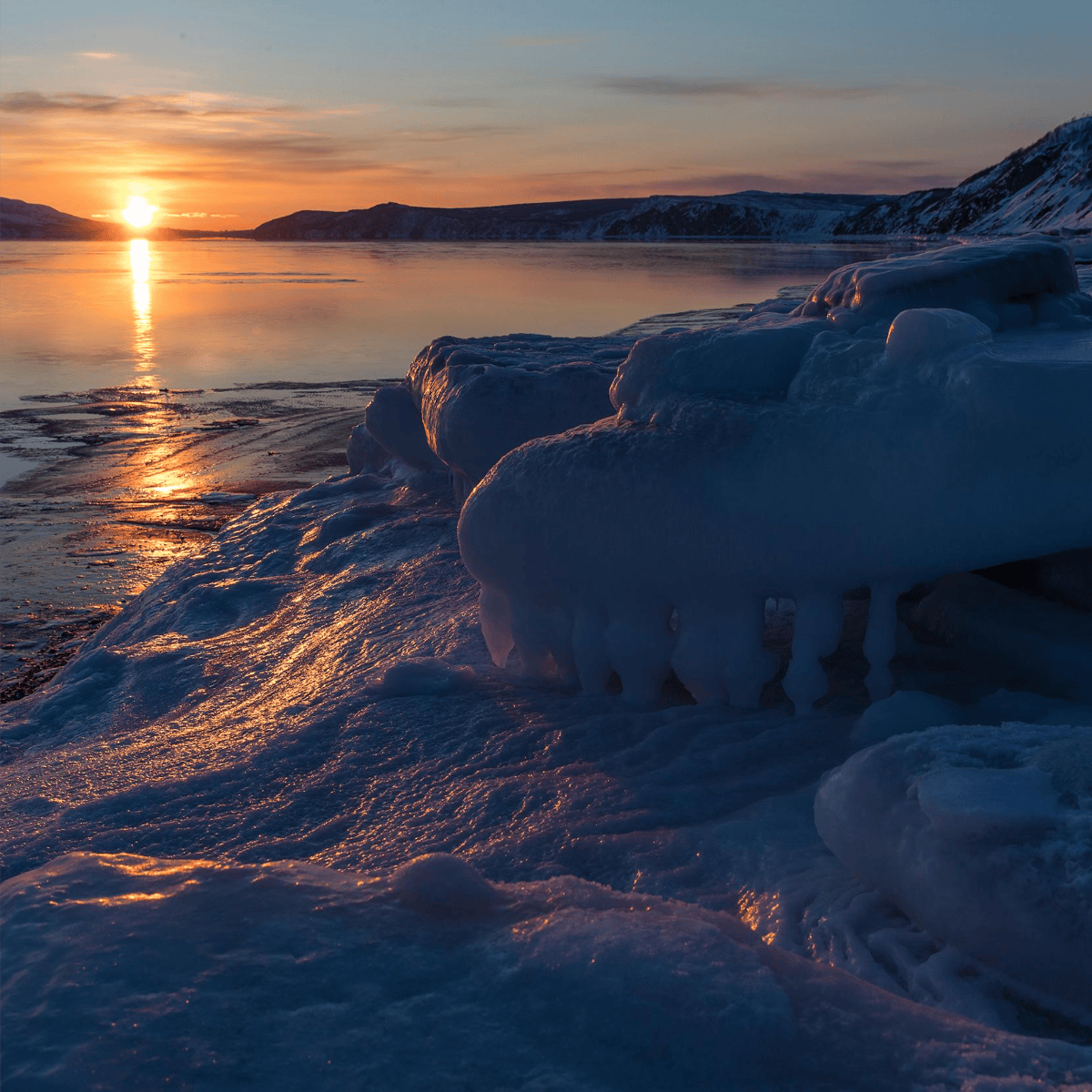 Sonnenaufgang über gefrorenem See mit eisigen Formationen am Ufer.