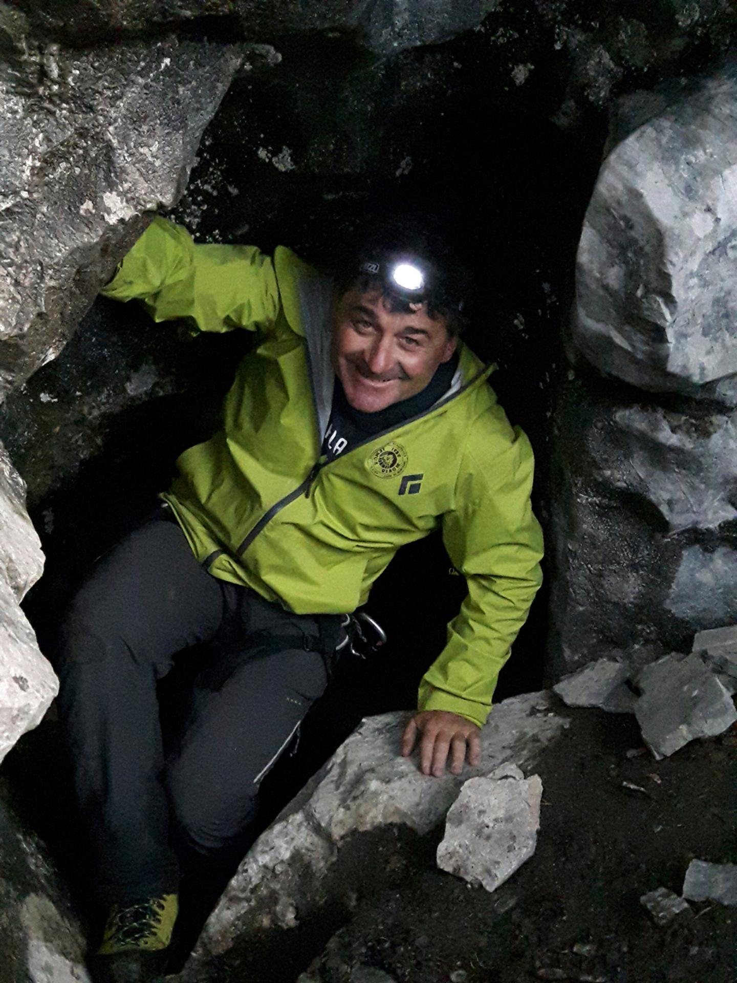 Ein Mann mit Stirnlampe klettert in einer Höhle durch Geröll.