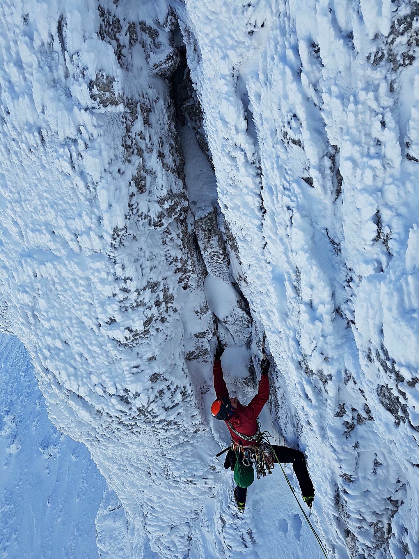 Eiskletterer in roter Jacke hangelt sich an vereister Felswand nach oben.