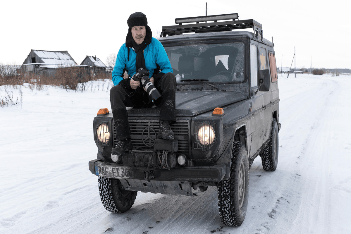 Zwei Bergsteiger mit blauen Helmen stehen auf einem verschneiten Gipfel vor einer Gebirgskulisse.