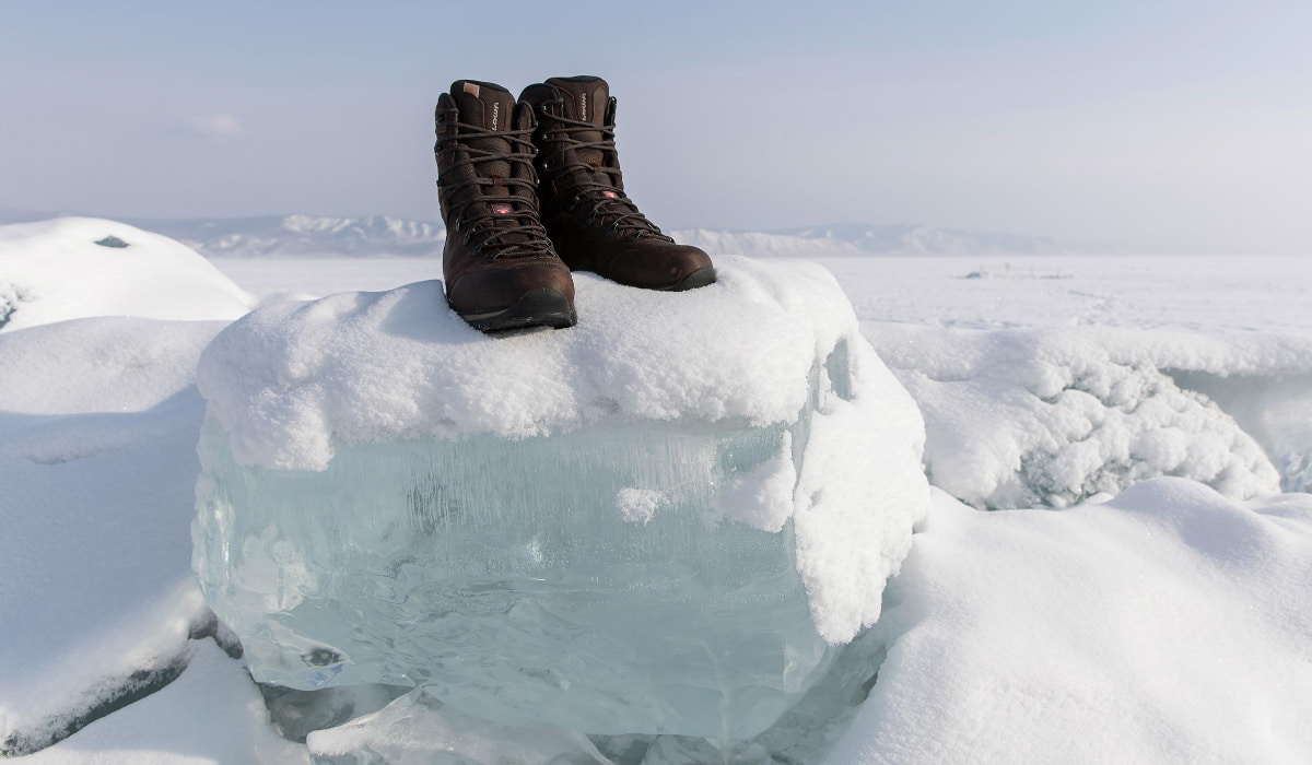 Braune Winterstiefel stehen auf einem Eisblock im Schnee auf einer gefrorenen Landschaft.