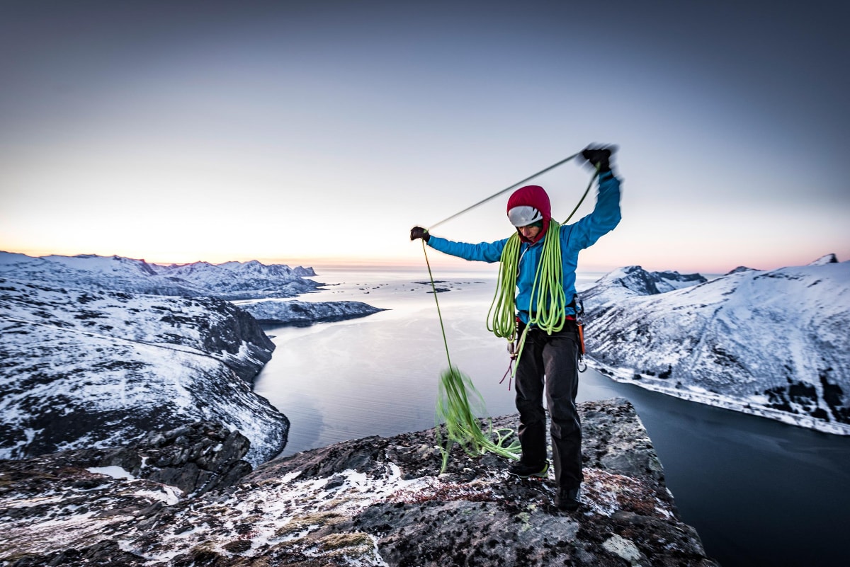 Female mountaineer preparing rope at icy fjord at sunset.