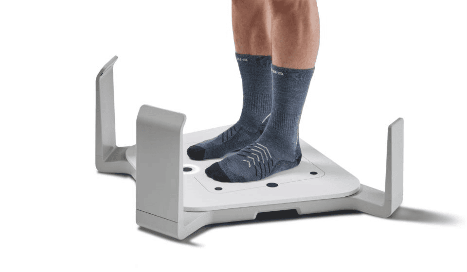 Ein Mann steht auf einer Messplattform, daneben wird auf einem Tablet eine Fußvermessung mit 3D-Modellen angezeigt.