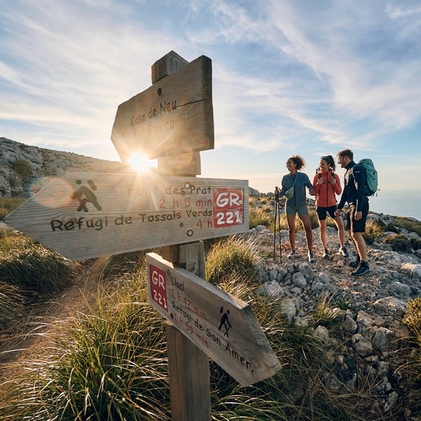 Three hikers at a signpost in the mountains with sunset and mountain scenery.