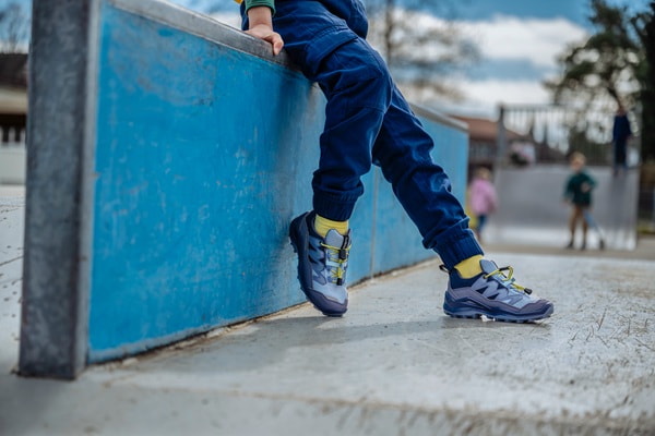 Füße in Wanderschuhen auf einem Baumstumpf mit Steinmauer im Hintergrund