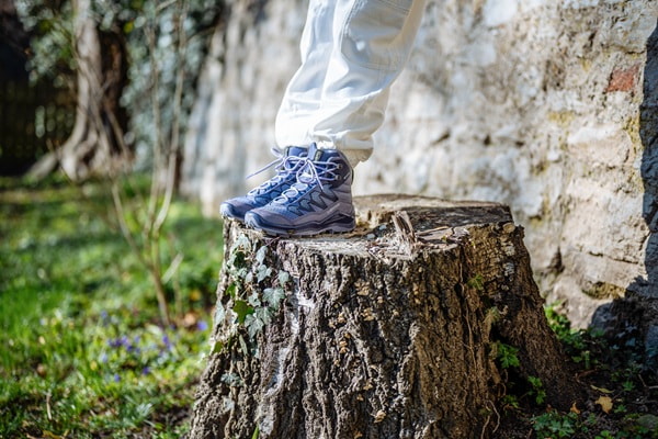 Füße in Wanderschuhen auf einem Baumstumpf mit Steinmauer im Hintergrund