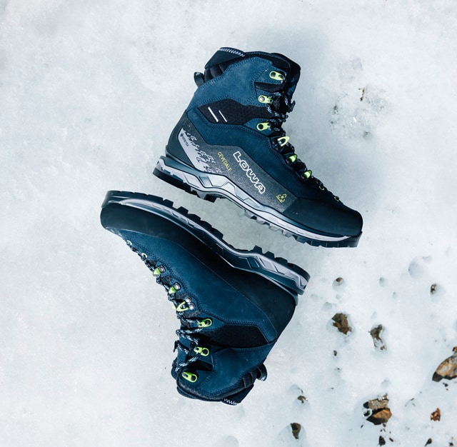 A person\'s bright blue hiking boots stand on a rock, showcasing outdoor equipment in a natural setting.