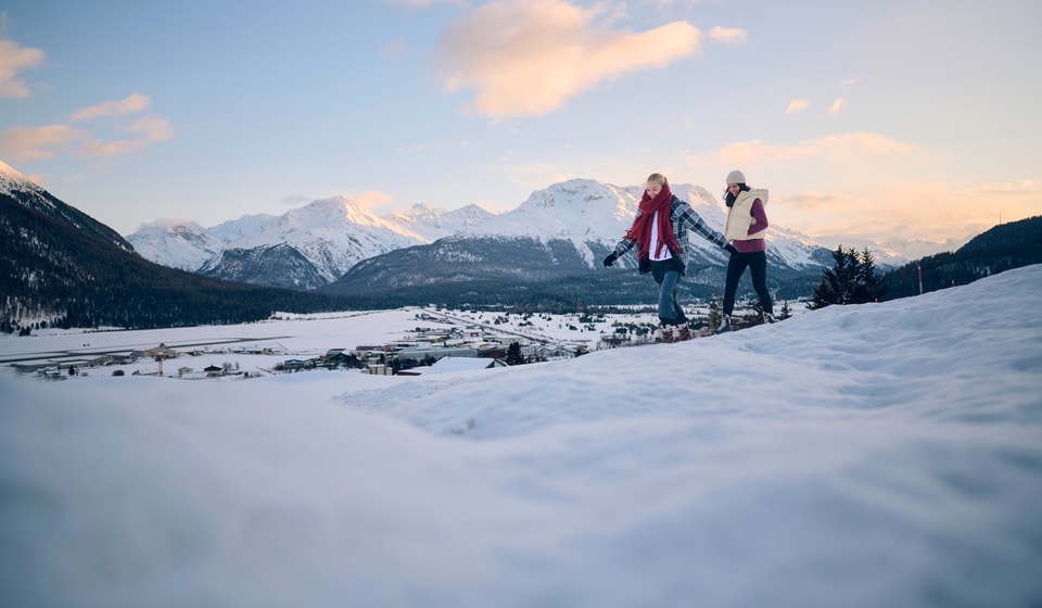 A man is hiking on a mountain peak, behind him stretch rock formations and a vast landscape.
