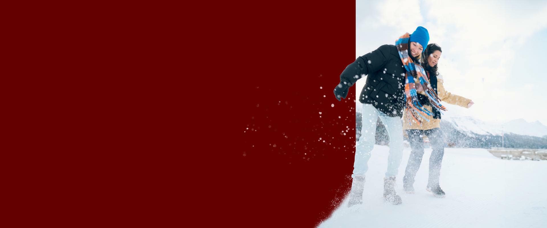 A couple joyfully stands in the snow, arms wide open, embracing the winter atmosphere.