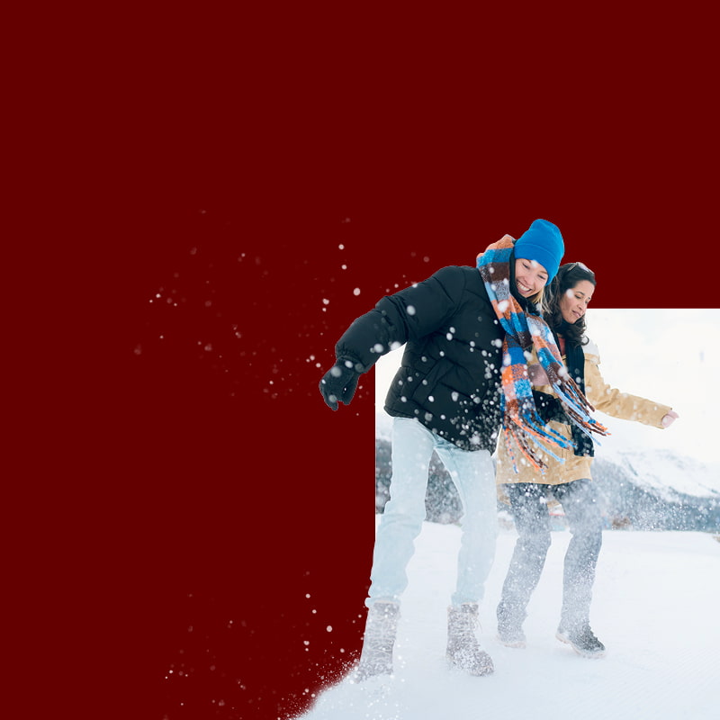 A couple joyfully stands in the snow, arms wide open, embracing the winter atmosphere.