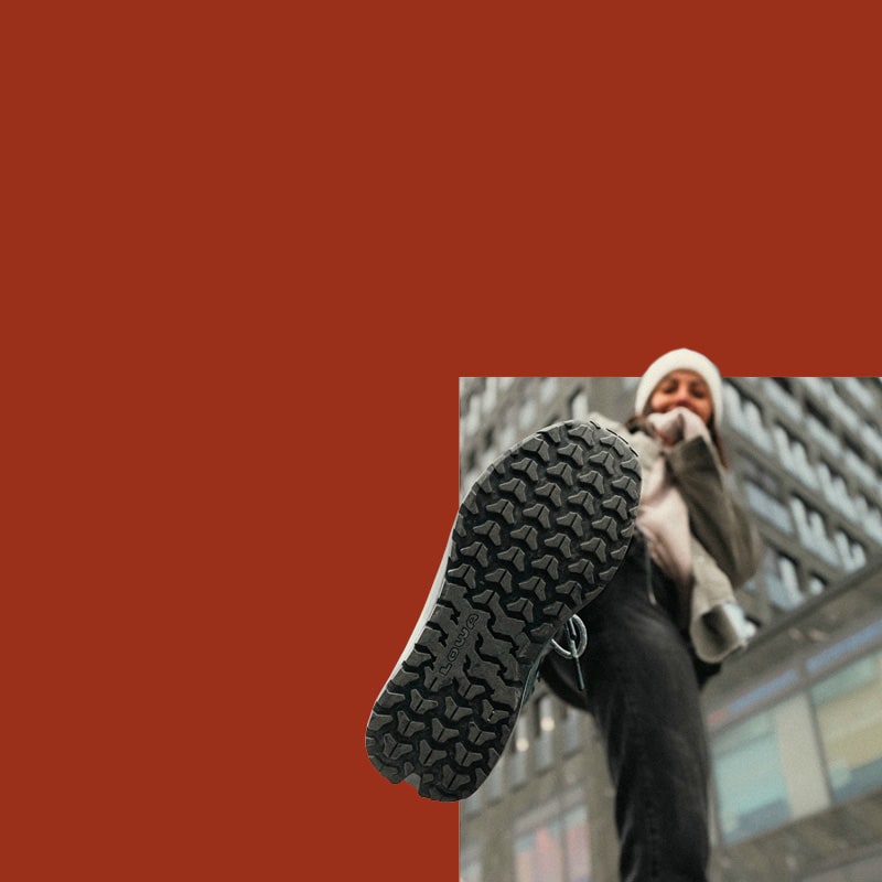 The image shows a person stepping forward wearing LOWA shoes. A building can be seen in the background.