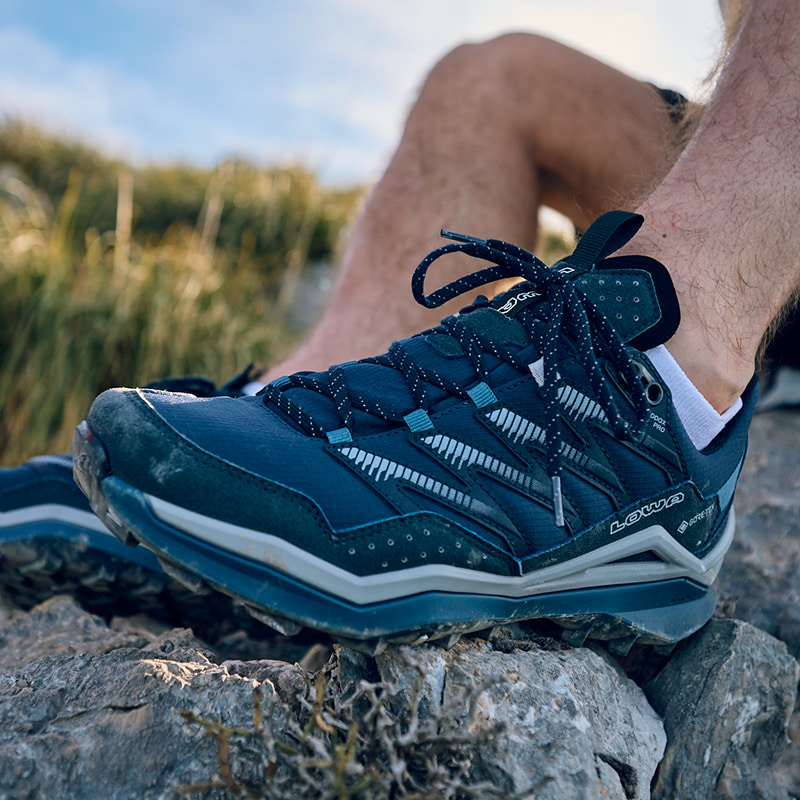 Close-up of a lightweight hiking boot on a rock, with short socks and legs.