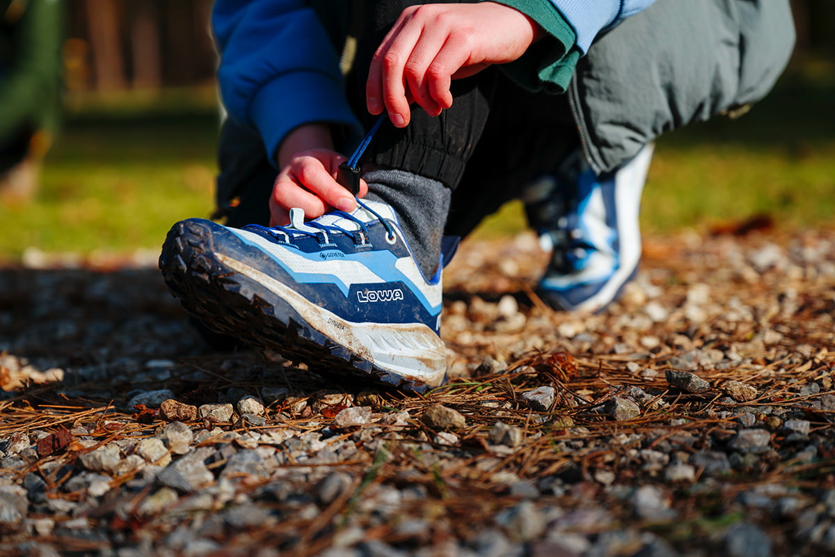 Lowa Wanderschuhe in altrosa mit orangefarbenen Schnürsenkeln, auf einer Wiese mit Blumen.