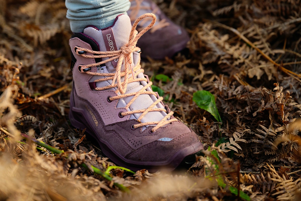 Lowa Wanderschuhe in altrosa mit orangefarbenen Schnürsenkeln, auf einer Wiese mit Blumen.