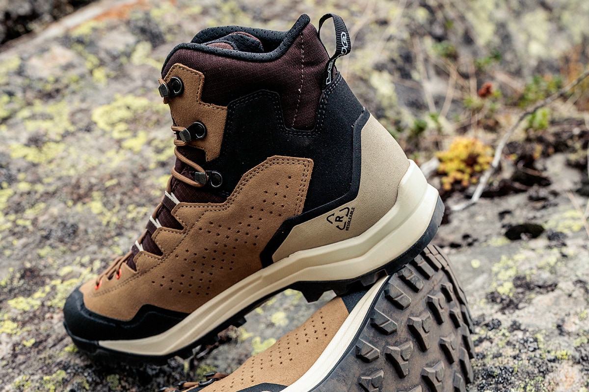 Fotografie eines braun-schwarzen Wanderschuhs auf felsigem Untergrund, der robuste Bauweise und Profilsohle für Outdoor-Aktivitäten zeigt. Details wie Metallösen, gepolsterter Schaft und markantes Sohlenprofil heben Funktionalität und Strapazierfähigkeit hervor.