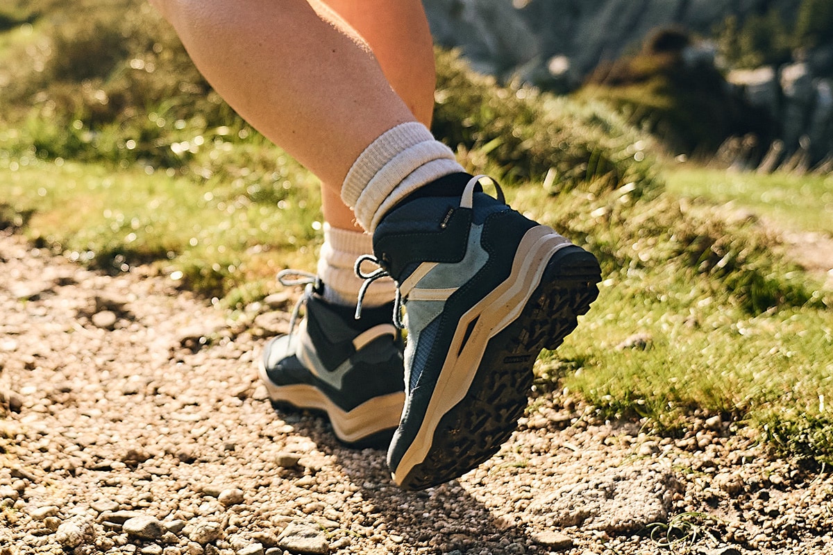 Wanderer in blauen Wanderschuhen auf einem steinigen Weg mit grünem Gras im Hintergrund.