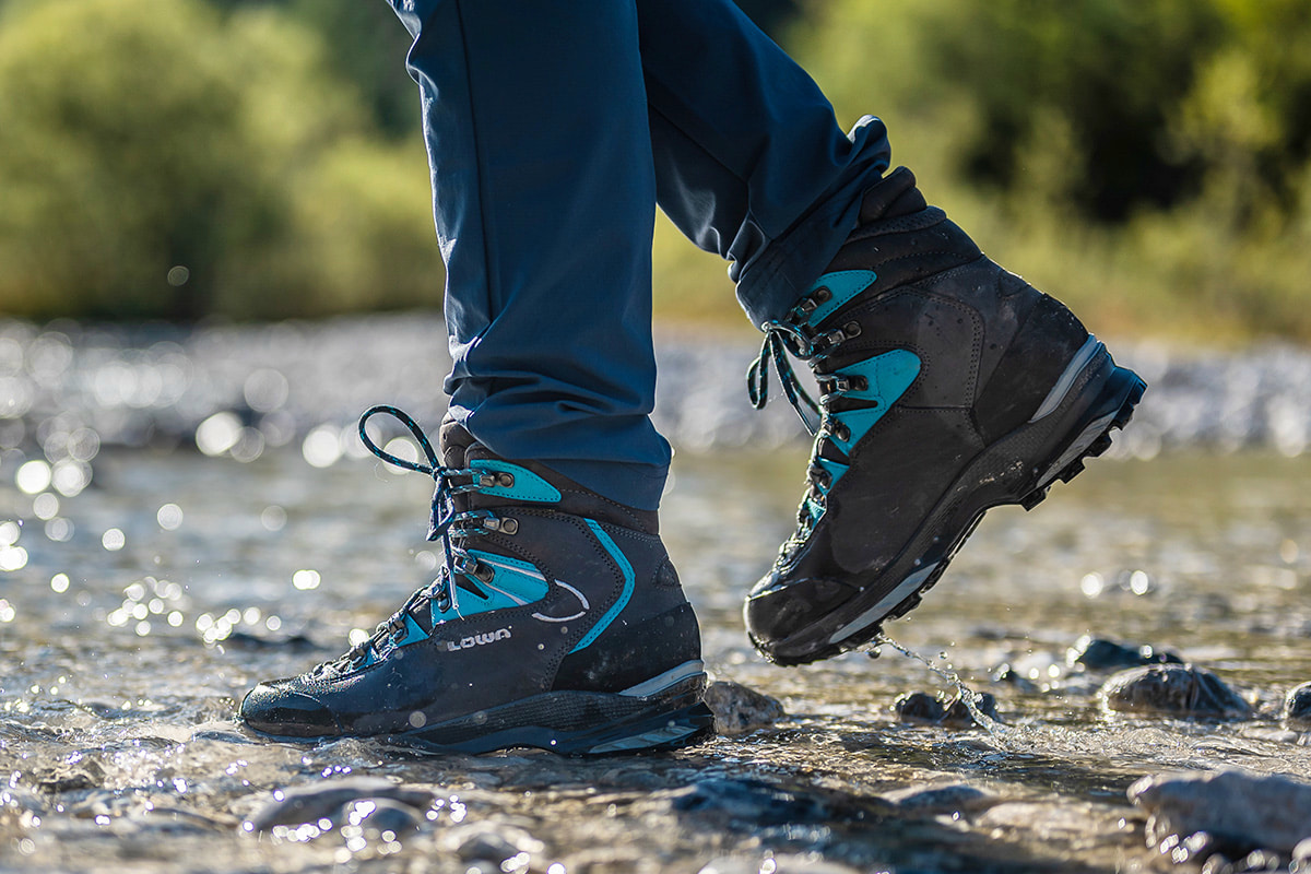 Nahaufnahme eines hellgrauen MADDOX PRO GTX LO SL der Marke Lowa auf felsigem Untergrund mit grüner Vegetation im Hintergrund. Fokus liegt auf robustem Design, stabiler Sohle und Schnürsystem, geeignet für Outdoor-Aktivitäten.