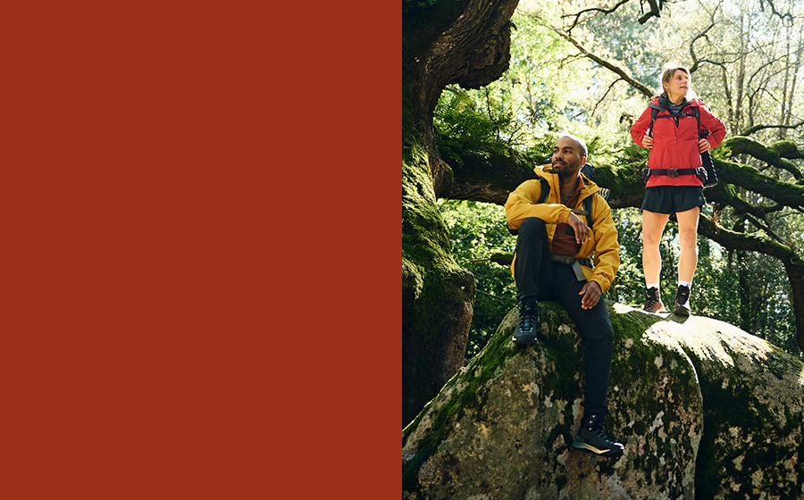 A man and a woman wearing hiking gear are sitting on a rock.